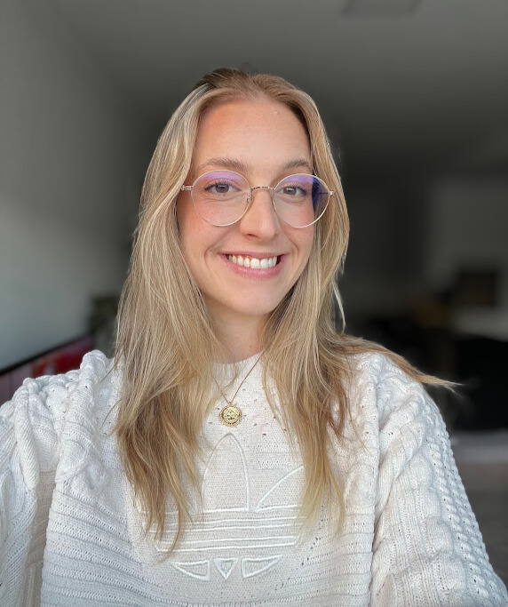 Foto da professora Amanda Seimetz sorrindo, com uma blusa verde e o fundo desfocado